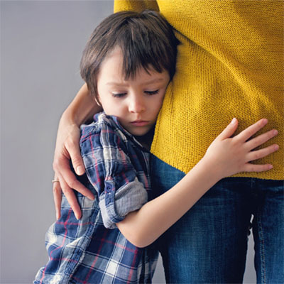 a young child with a forlorn expression clings to his mother who has her arm around him.